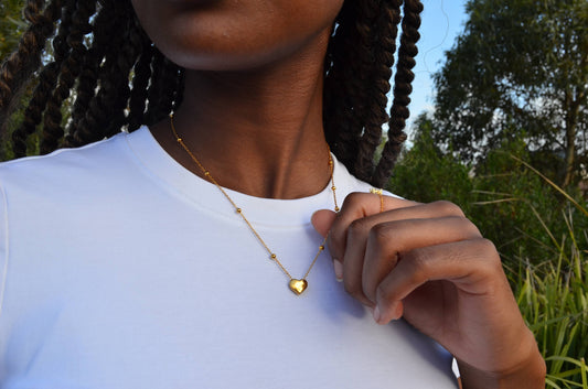 Gold chain necklace with a small gold heart-shaped pendant and small gold spheres evenly along the chain, worn on a girl