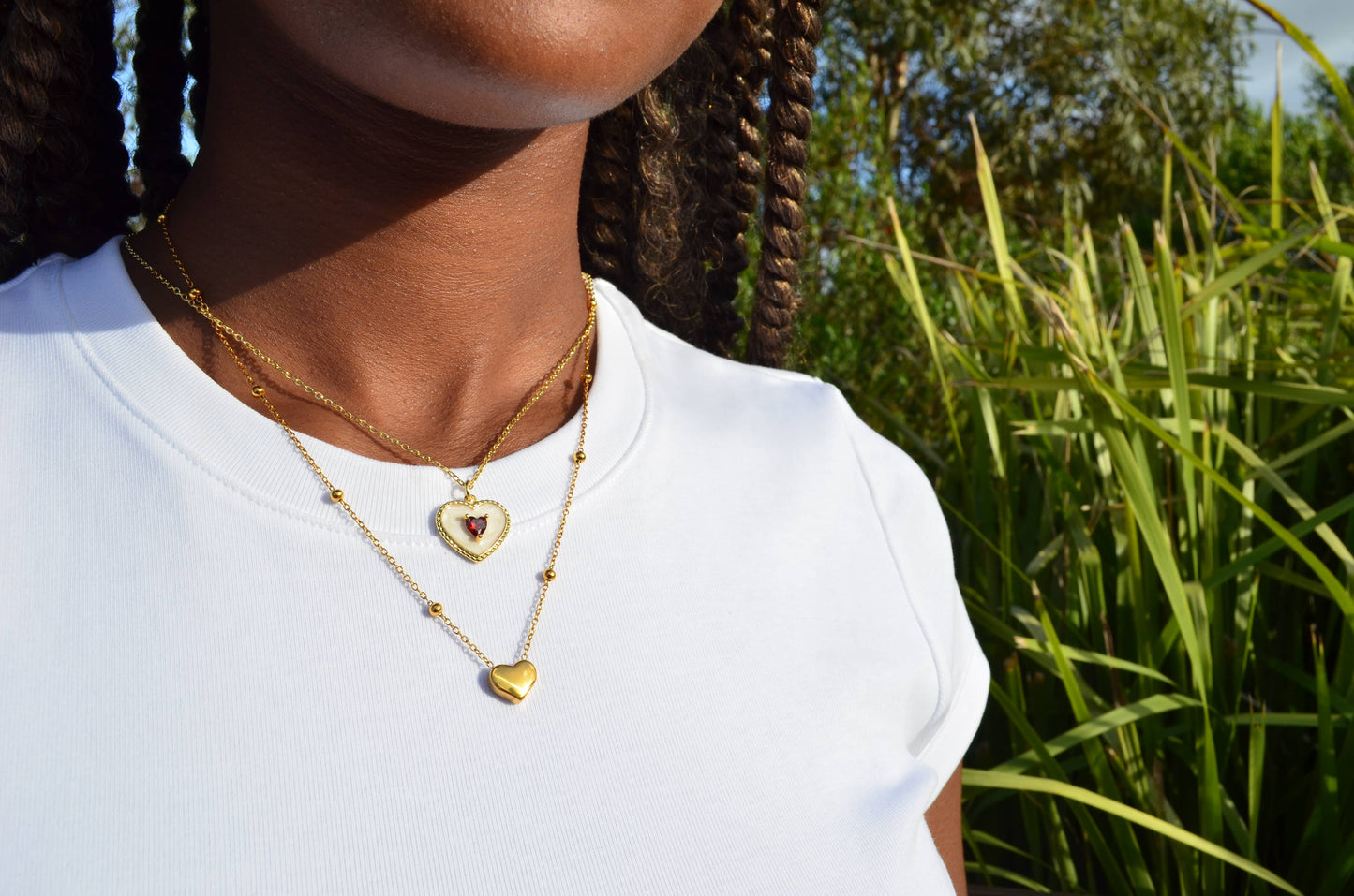 A gold and white heart-shaped pendant necklace with a red heart-shaped gem set in the centre, worn on a girl with The Afsanas Heart Necklace