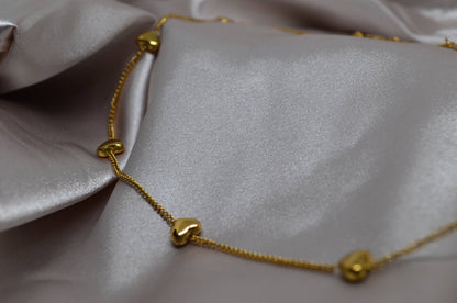 Close-up of a gold chain necklace with small heart-shaped motifs spaced out evenly along the chain