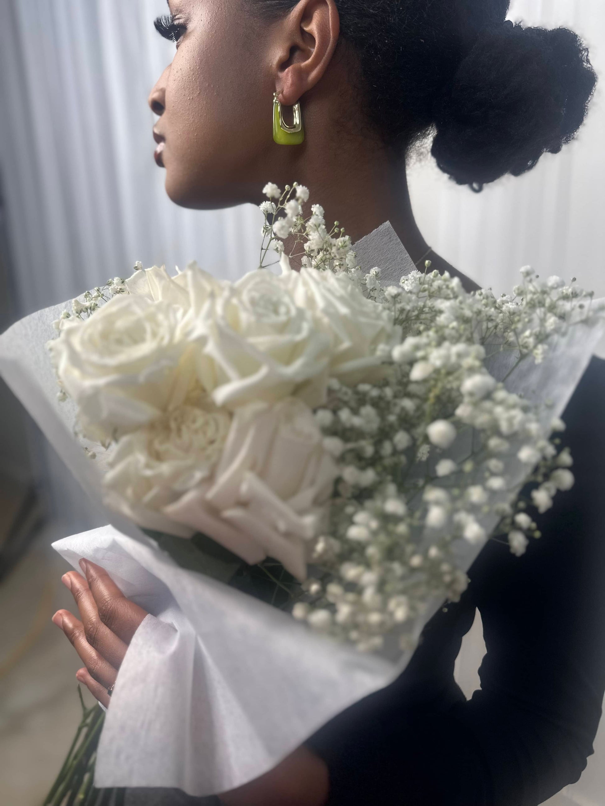 Green rectangular earrings with gold hardware worn on a girl holding white flowers