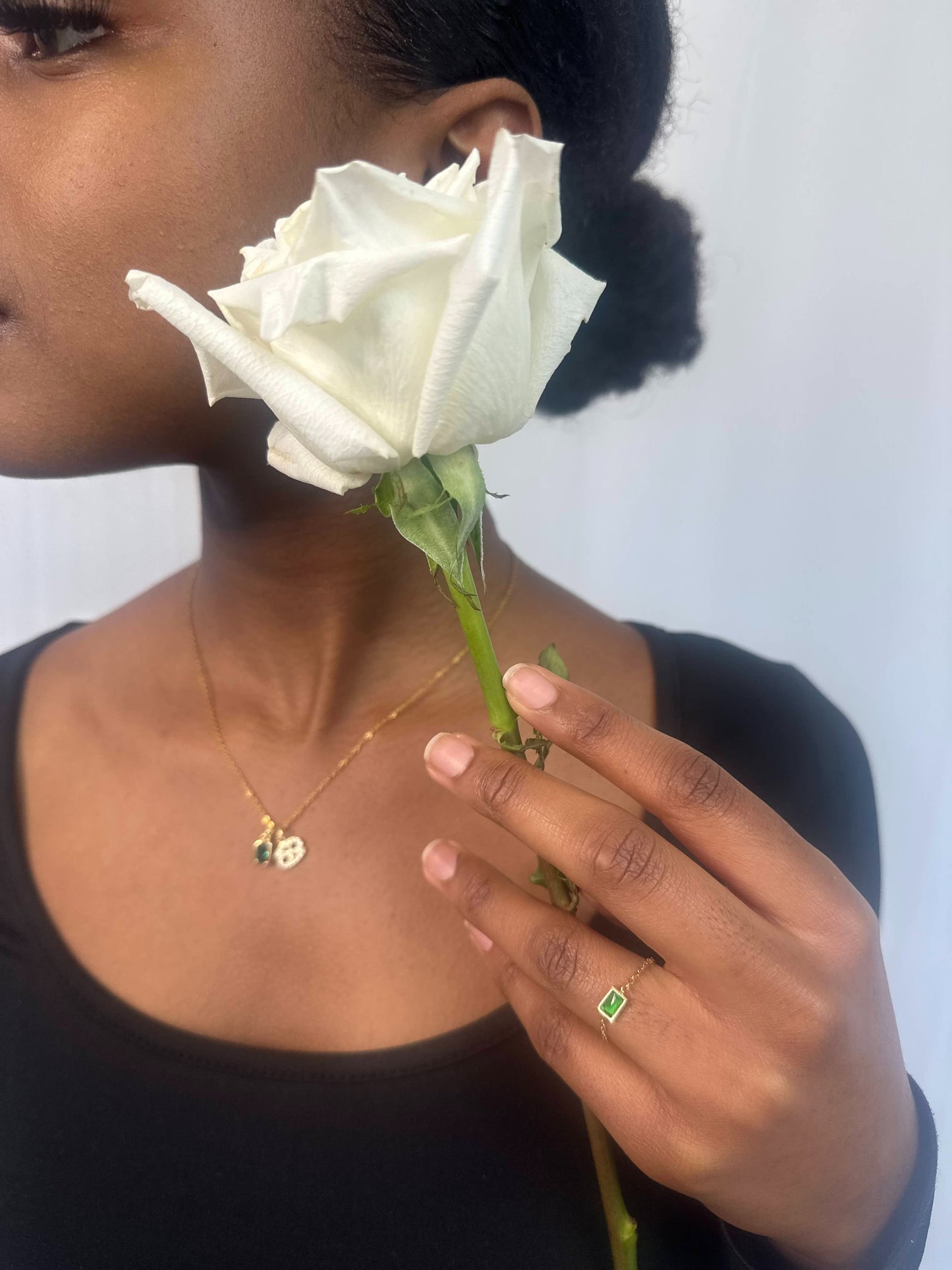 Adjustable thin gold ring with a gold sphere adjuster featuring rectangular green gem and Horoscope Necklace worn by a girl holding a white flower