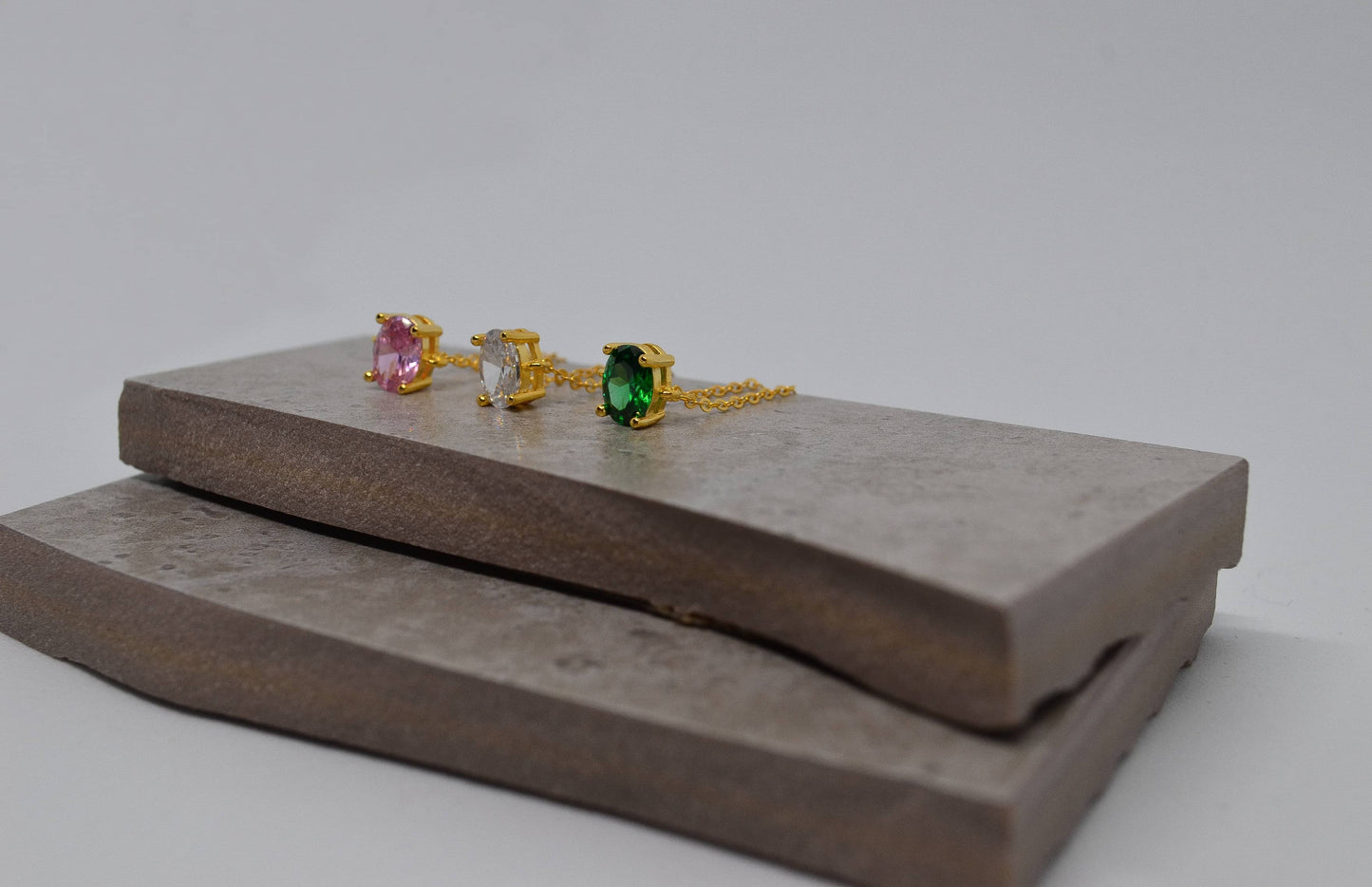 Three adjustable thin gold chain adjustable rings with pink, white and green oval gems respectively