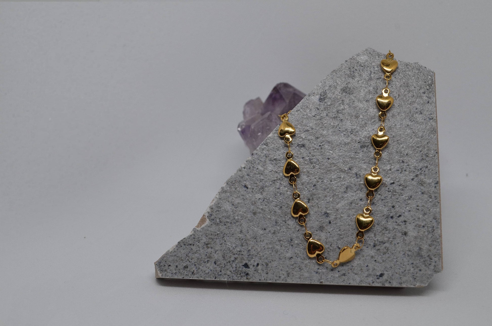 A gold heart-shaped chain necklace displayed on an amethyst crystal slab