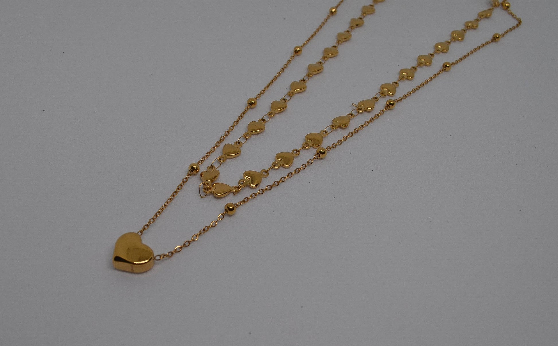 A gold heart-shaped chain necklace displayed with a small gold heart-shaped pendant necklace