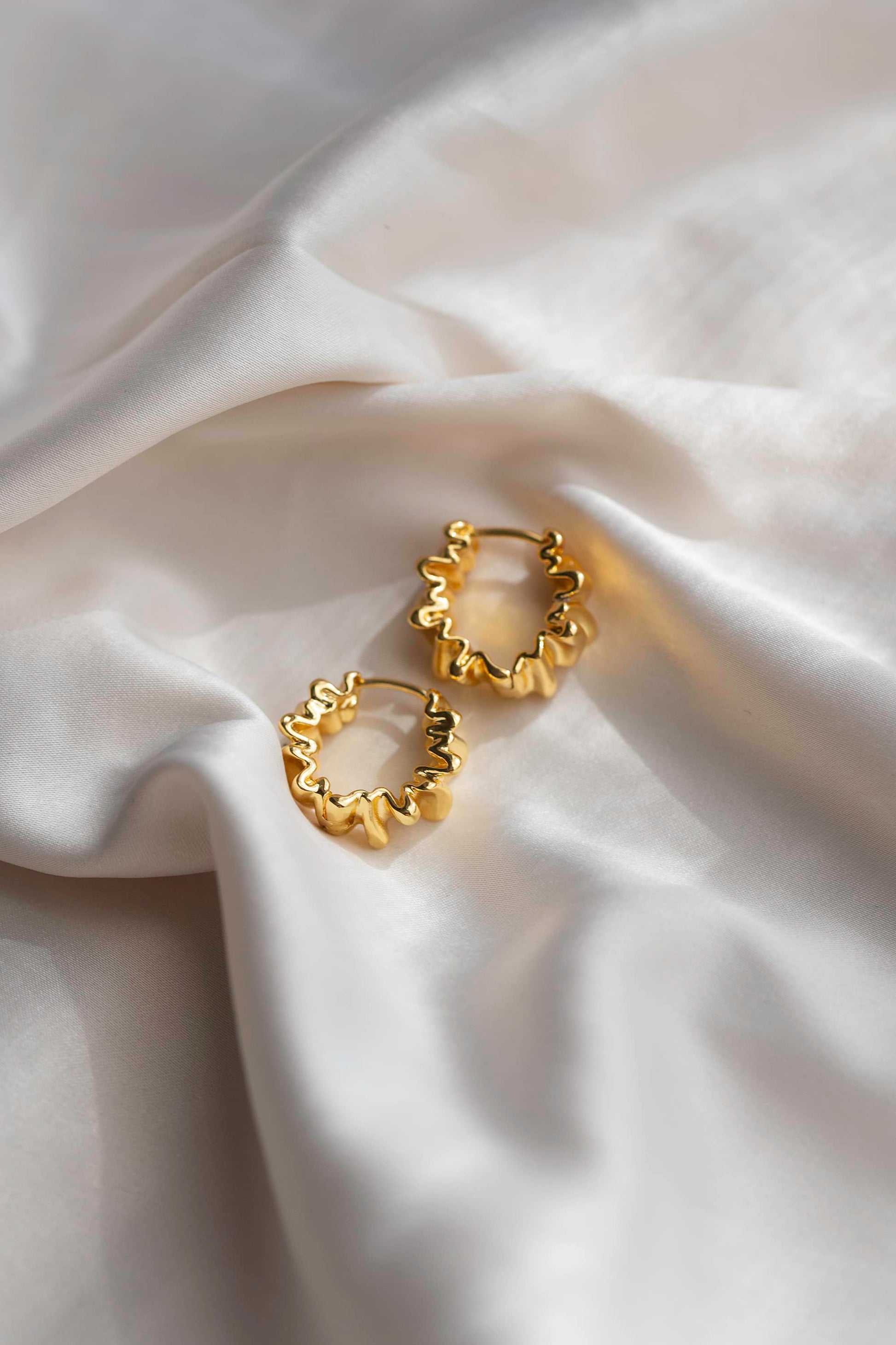 Abstract gold hoop earrings displayed on silk