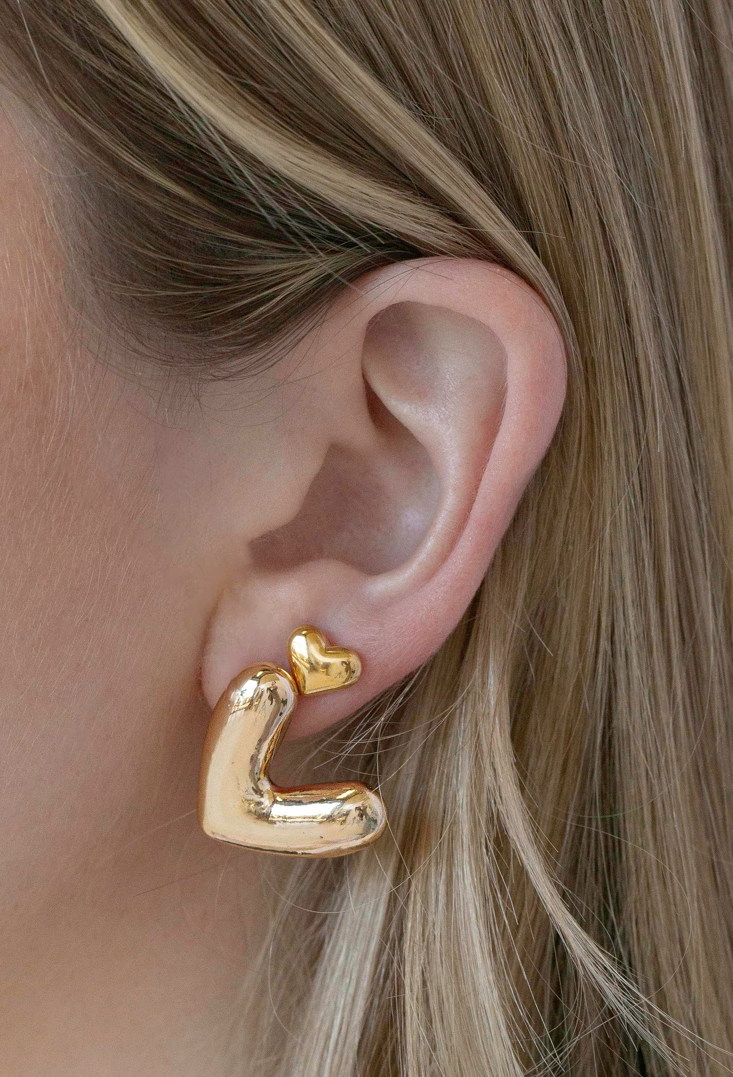 Thick heart-shaped gold stud earrings and small heart-shaped gold stud earrings stacked on model