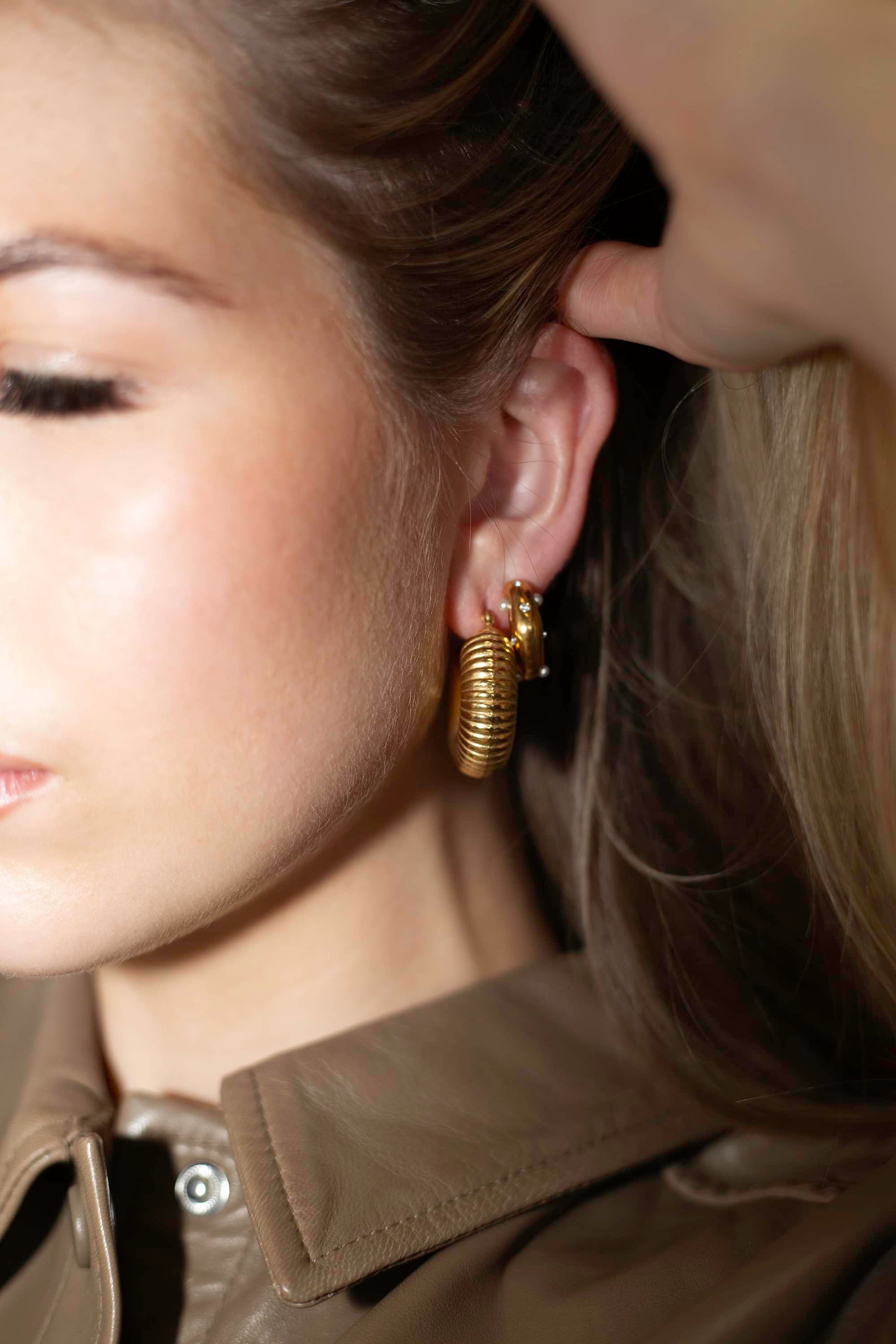 Close-up of thick gold coil hoop earrings, stacked on a model with The Daneens