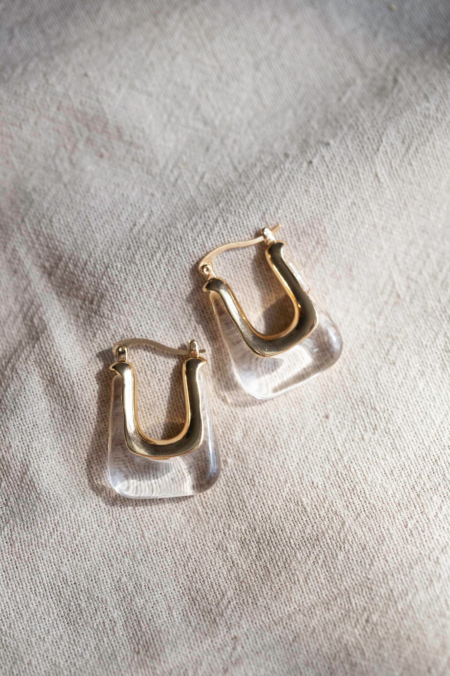 Clear rectangular earrings with gold hardware, displayed on linen